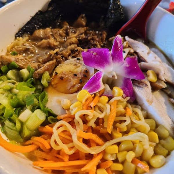 Close-up of Roc N Ramen bowl with noodles, meat, egg, corn, carrots, green onions, and an orchid.