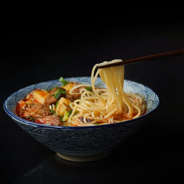 Chopsticks lifting noodles from a bowl of Roc N Ramen with beef and tofu.
