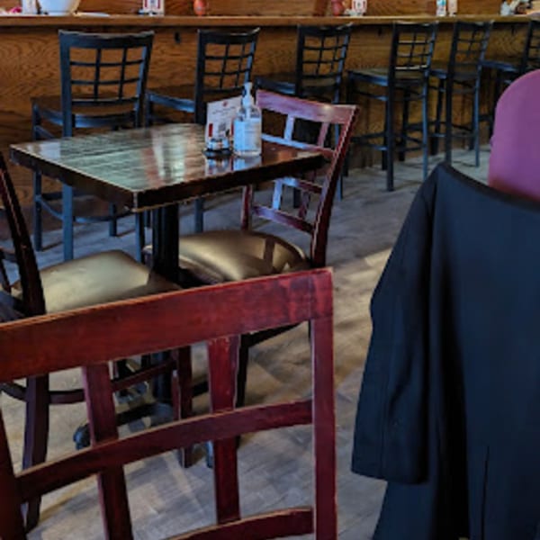 Empty dining area with wooden tables and chairs, and bar stools at a counter.