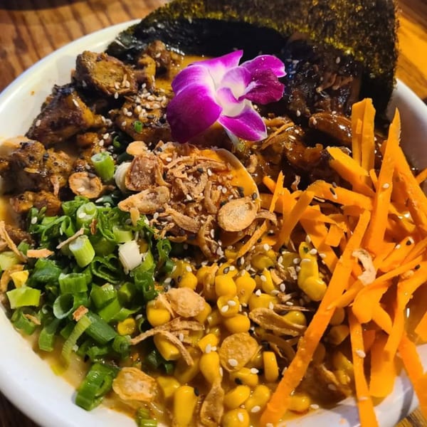 A colorful bowl of Roc N Ramen with chicken, corn, carrots, scallions, and a purple orchid.