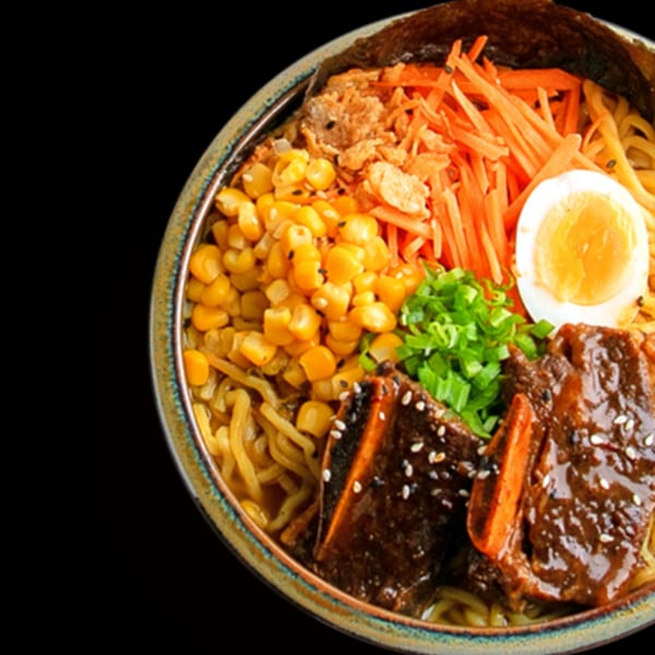 A close-up of Roc N Ramen's ramen bowl with noodles, corn, carrots, egg, and short ribs.