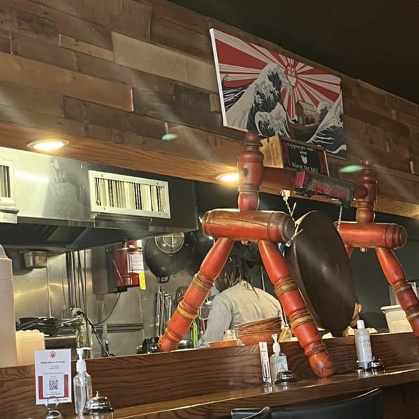 A Roc N Ramen kitchen with a chef, a Japanese art print, and red decorative elements.