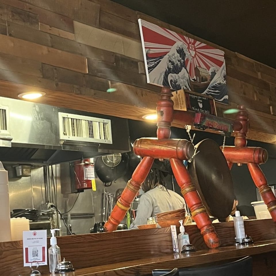 A Roc N Ramen kitchen with a chef, a Japanese art print, and red decorative elements.